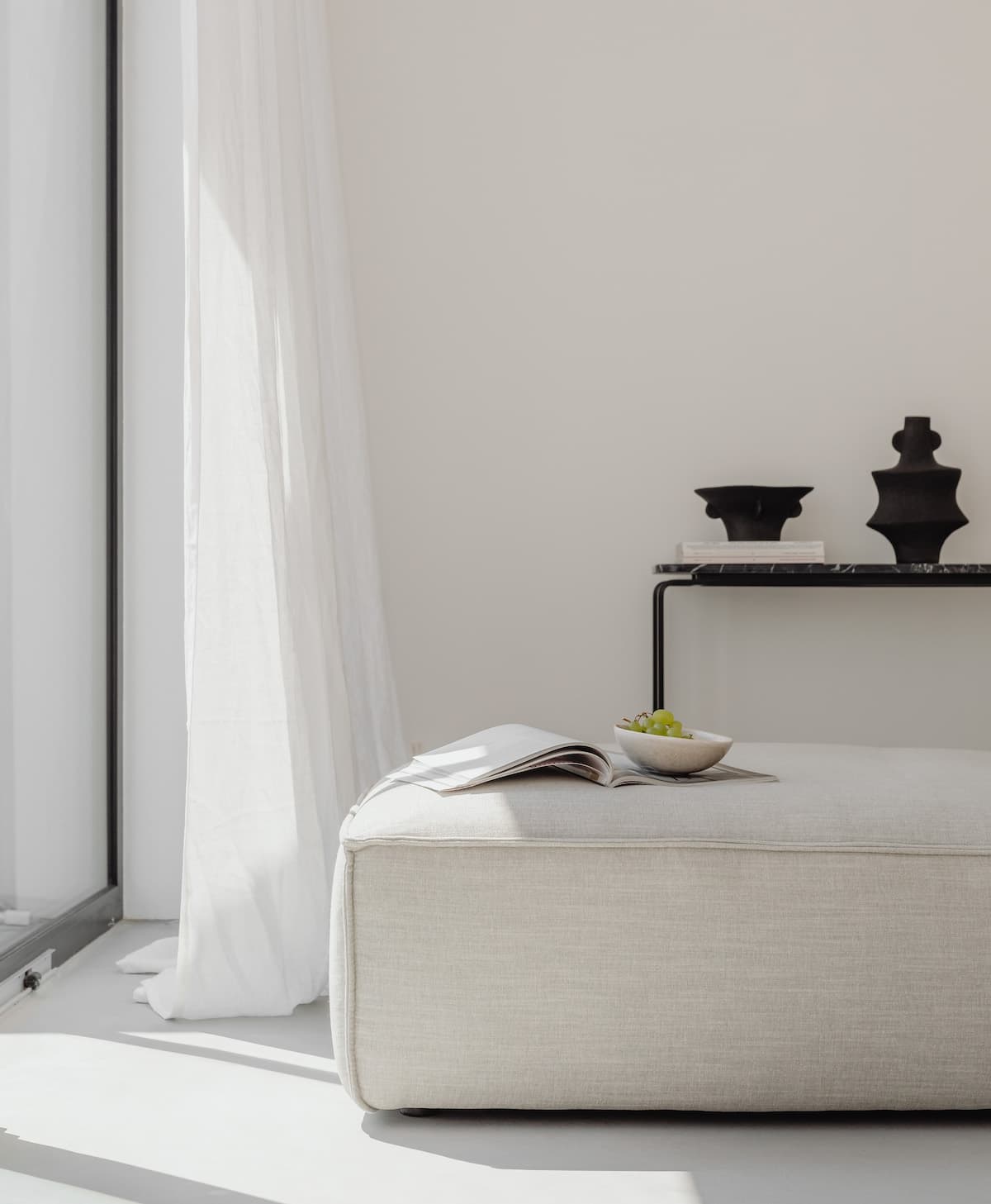 Gemütlich minimalistische wohnen mit weniger: ein bequemes Leinensofa, Leinenvorhänge, die das Tageslicht dämpfen und ein Keramikvasaen
