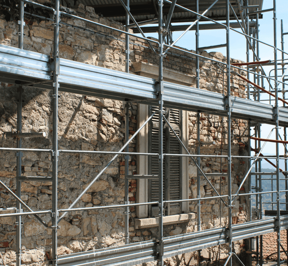 Baugerüst vor einem alten Haus mit Fensterläden, das gerade saniert wird