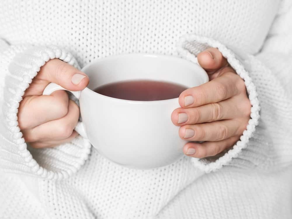 Frau mit einem weißen kuscheligen Pullover und mit einer Teetasse in der Hand. Sie macht einfach Pause.